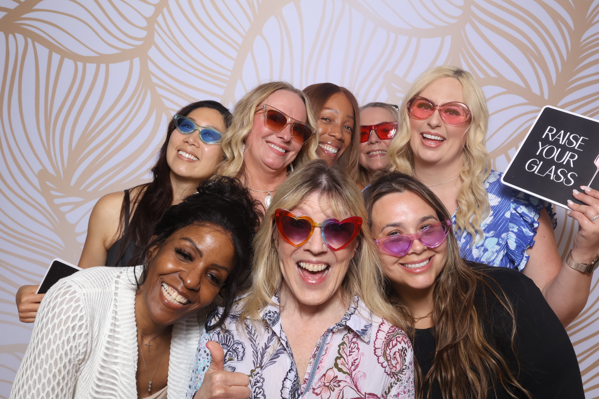 A group of guests posing with sunglasses and props in front of the golden leaves backdrop.
