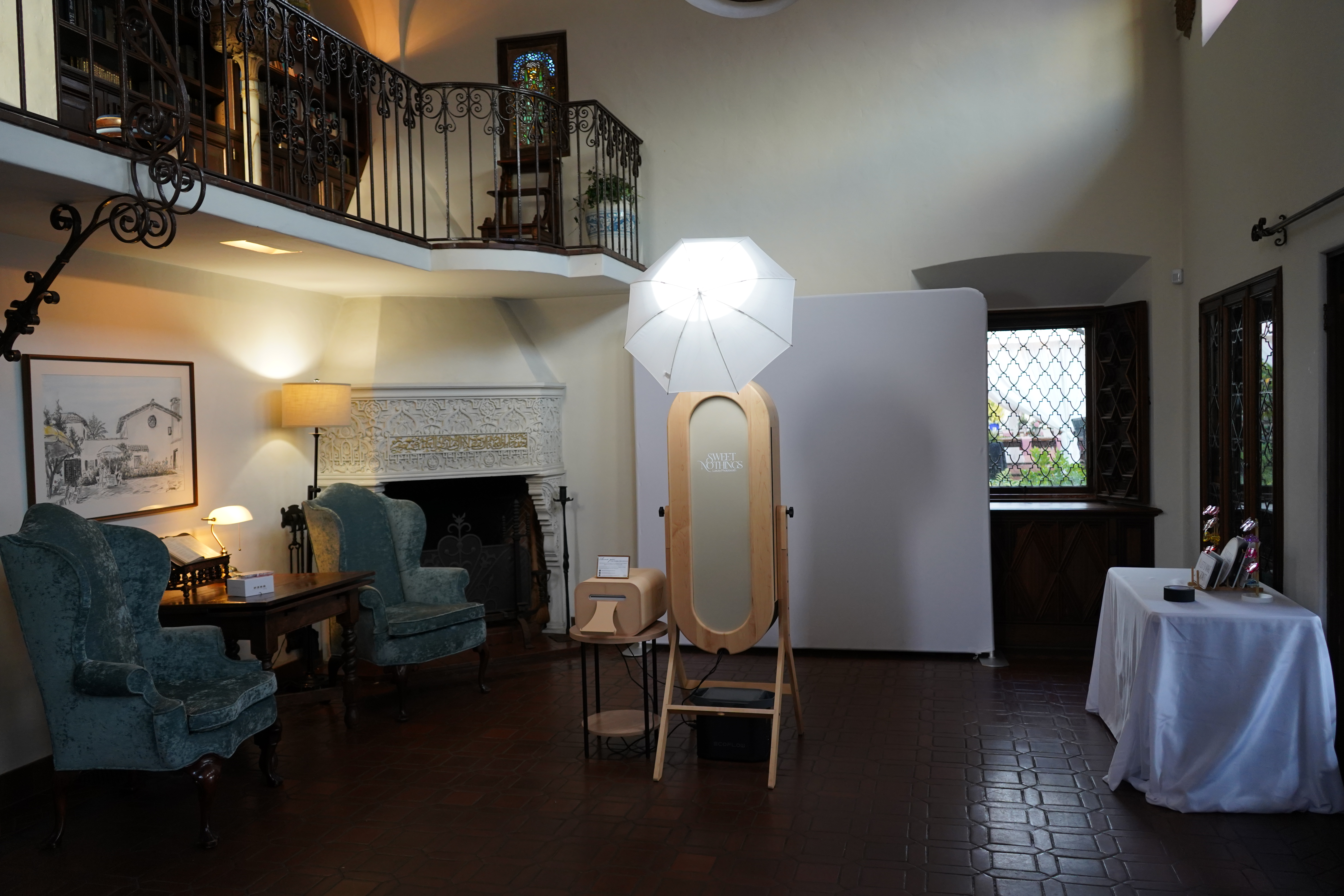 An elegant wedding reception venue with long wooden tables decorated with greenery, white candles, and neatly arranged glassware, set inside a spacious hall with tall wooden beams, skylights, and large windows.